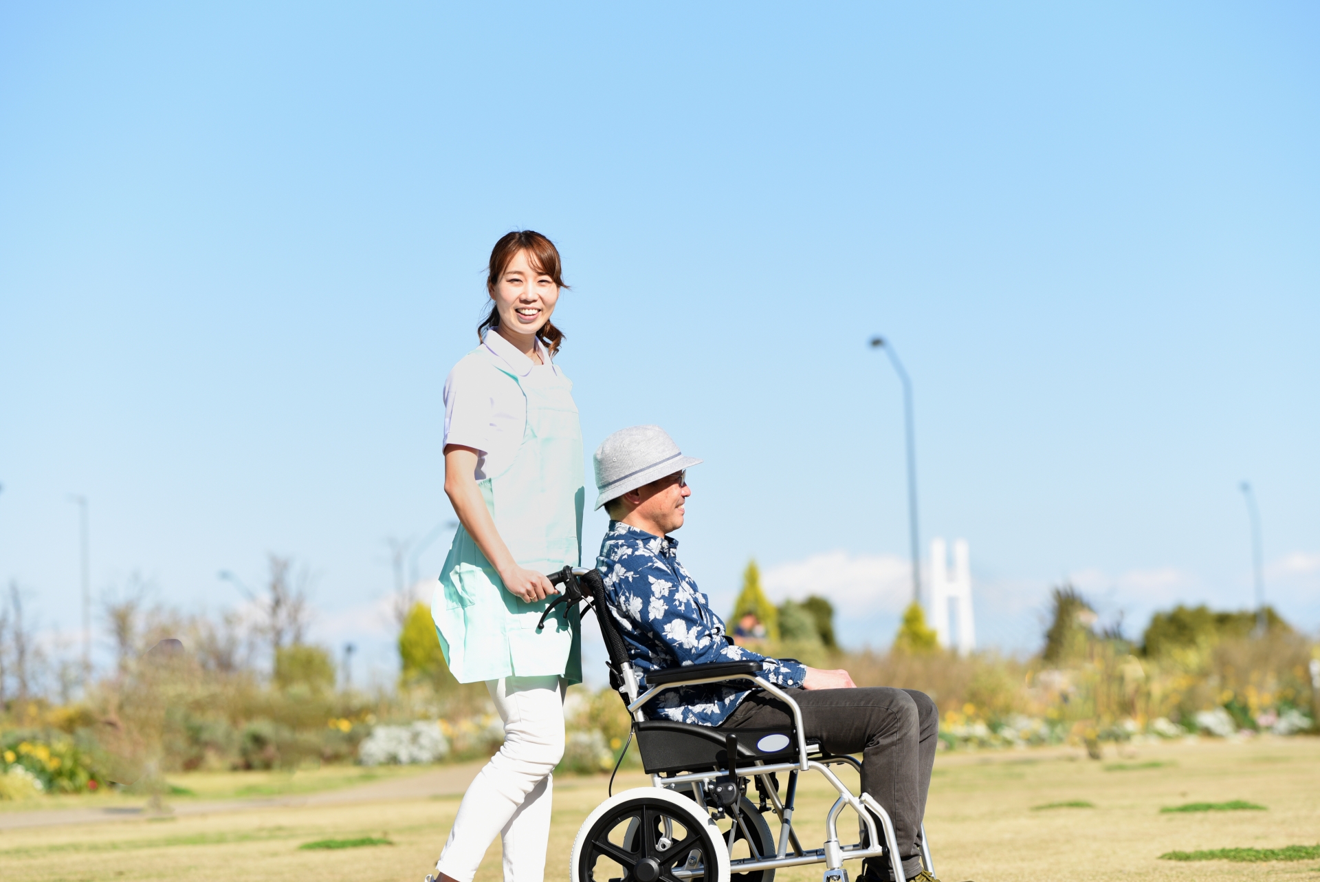 空の屋外で車椅子を押す若い介護士の女性とシニア男性