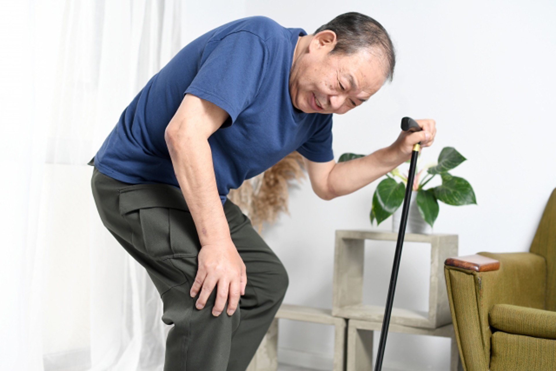 膝を押さえながら杖をつく高齢者男性