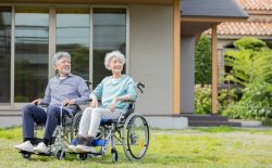 住居の前で車椅子に乗るシニア夫婦
