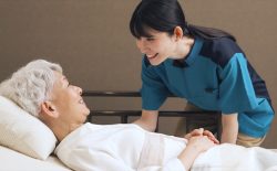 ベッドに横たわる老人女性に話しかける女性介護士