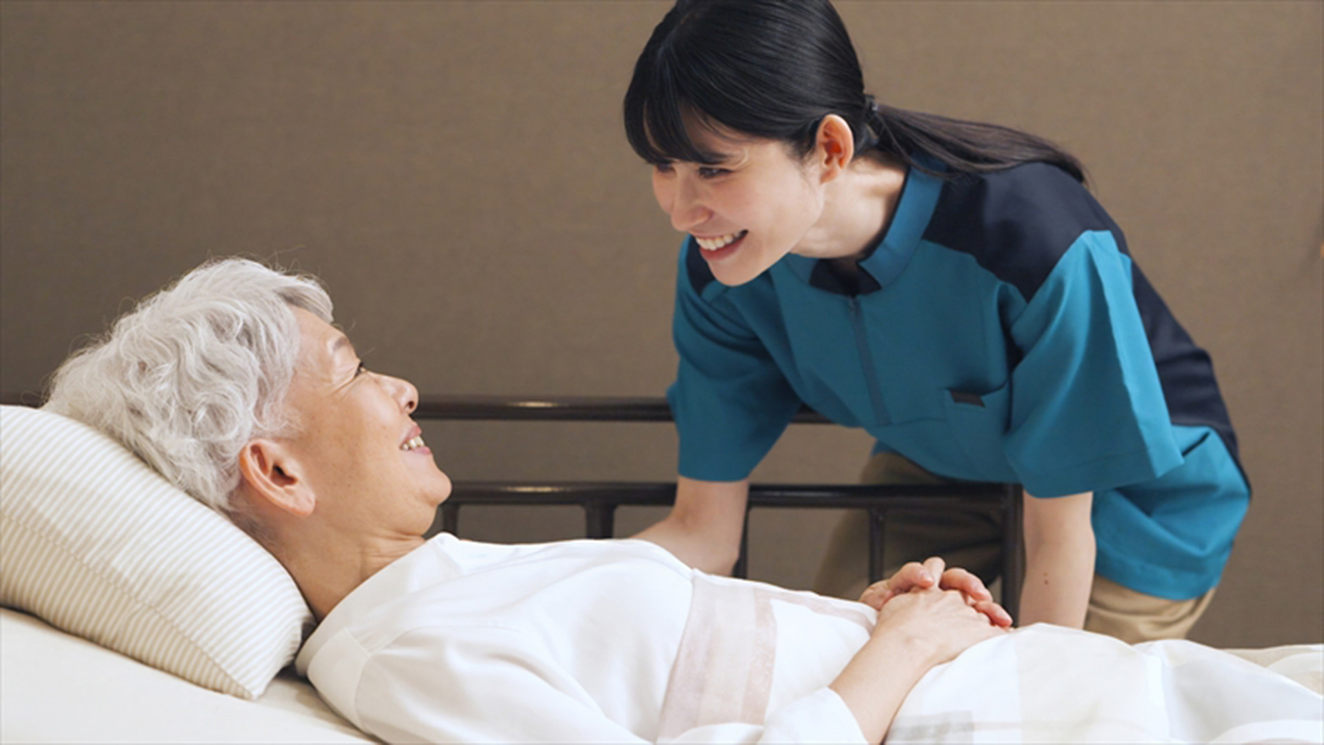 ベッドに横たわる老人女性に話しかける女性介護士